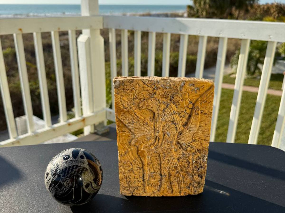 Stone carving and black ball on table, with ocean and palm trees in background.