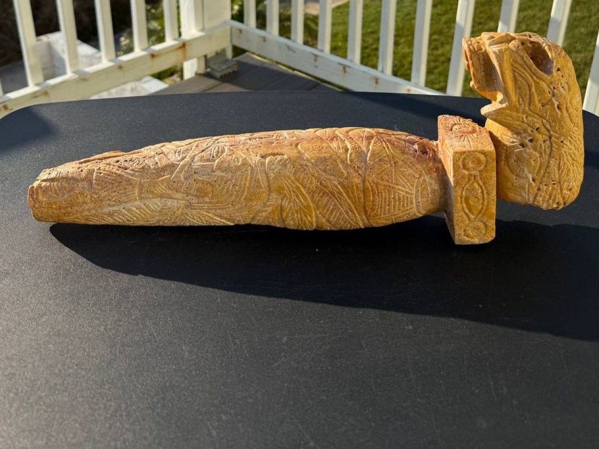 Intricately carved stone dagger with animal motifs on a dark surface, background of white railing.