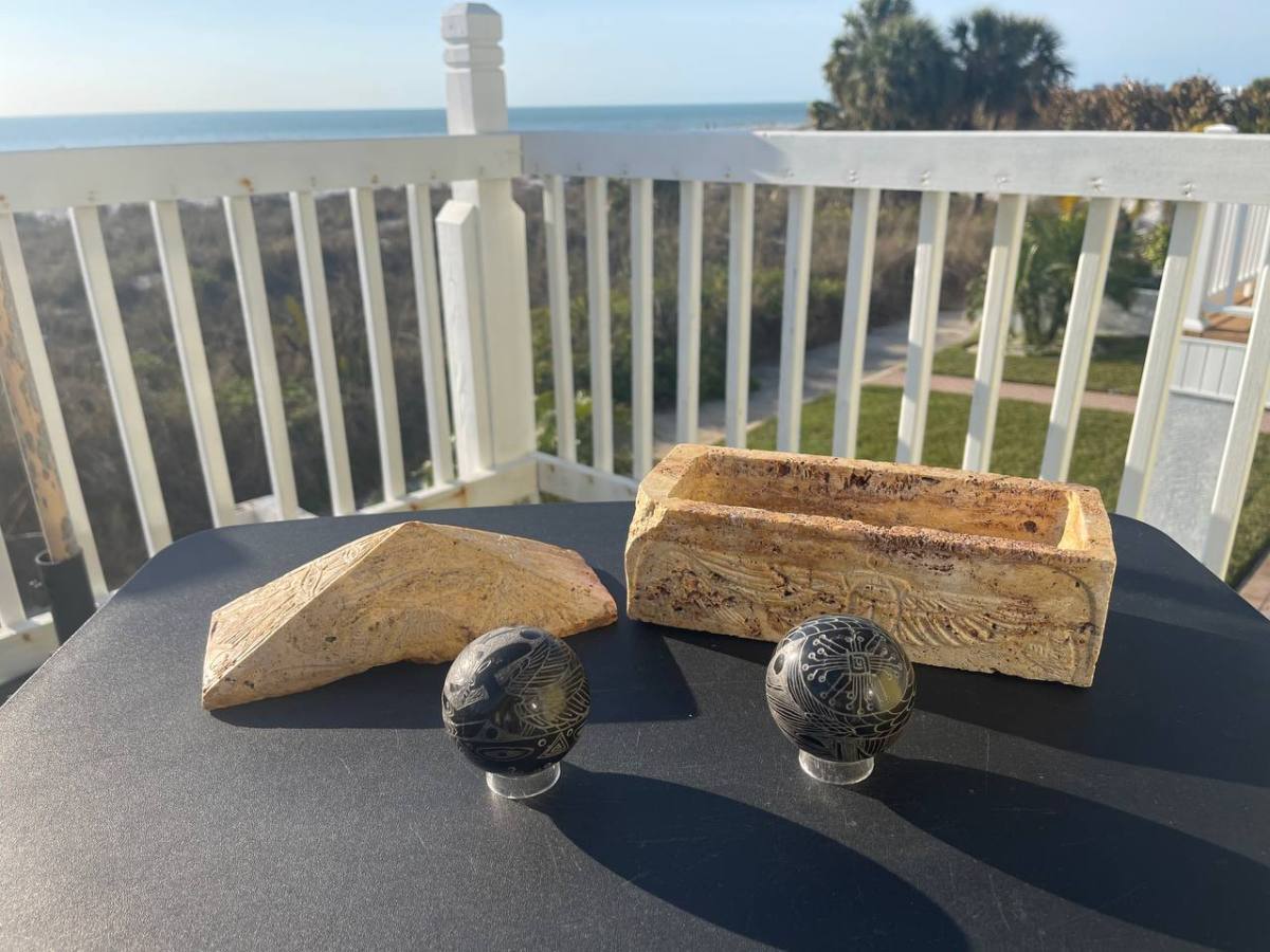 Two decorative stones and two engraved spheres on a table with ocean view and railing.