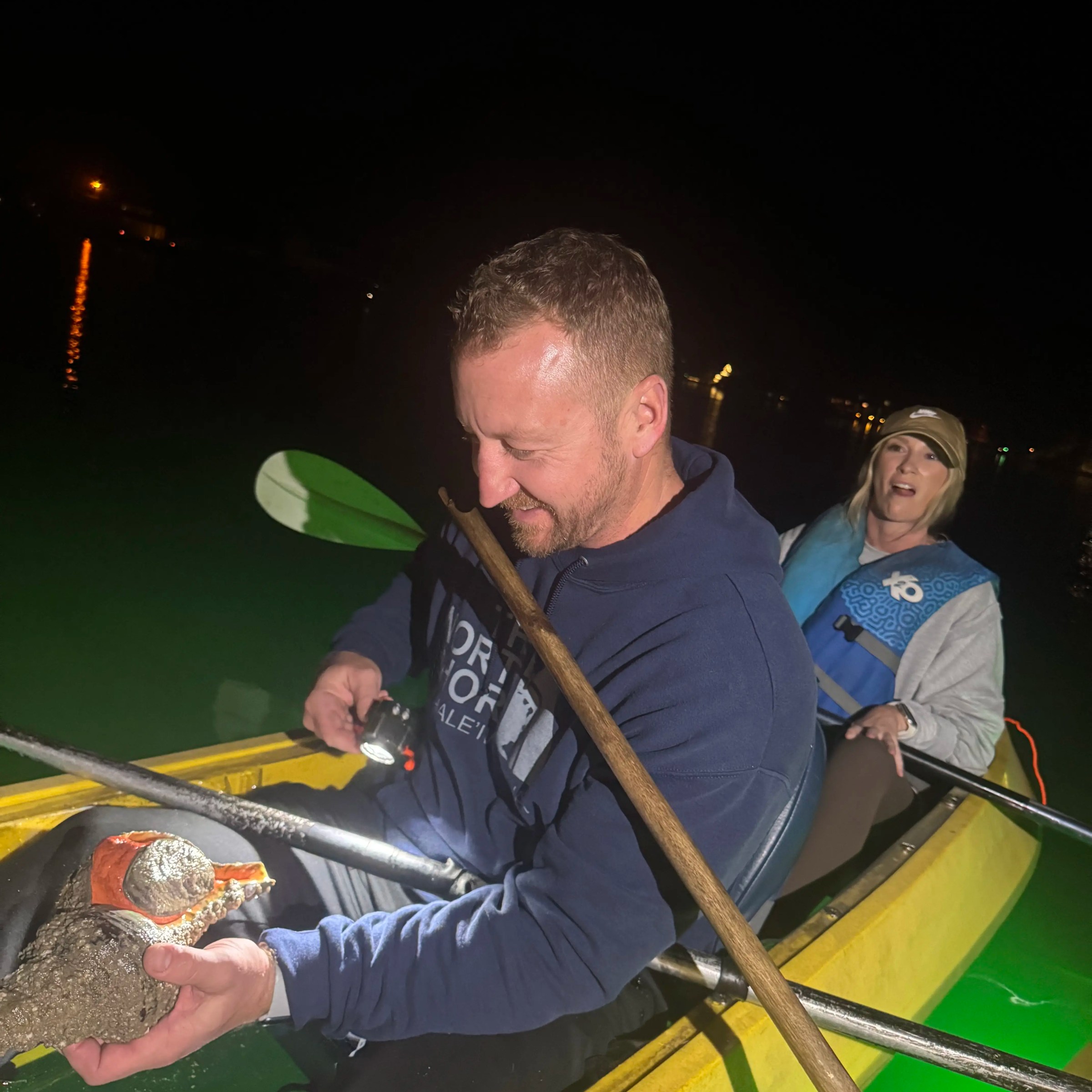 Two people in a kayak at night, one holding a small alligator.