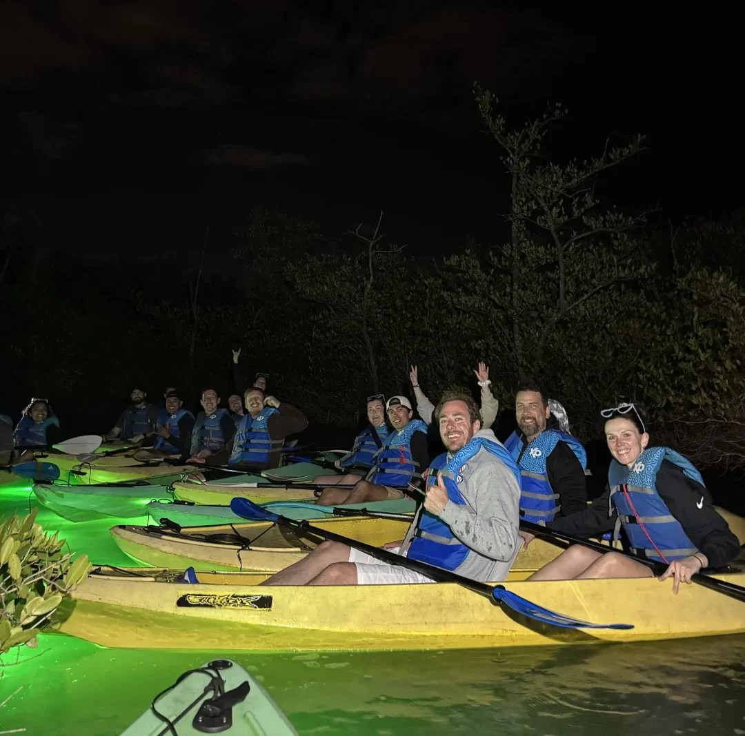 Group of people kayaking at night with glowing paddles.